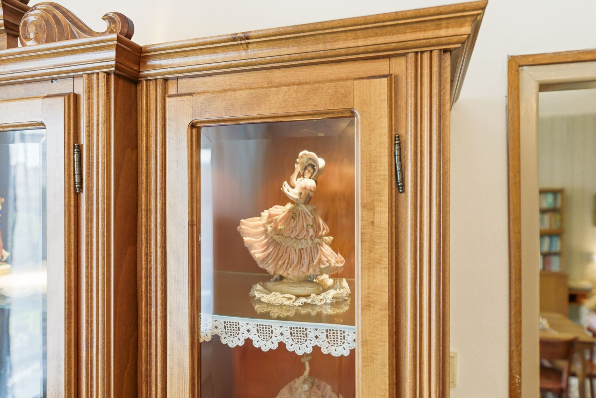Porcelánová figúrka dámy v dobových šatách vystavená v drevenej vitríne ako dekorácia pre automatický koncept interiéru.
