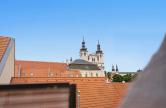 Historické kostolné veže týčiace sa nad strechami mesta pod modrou oblohou